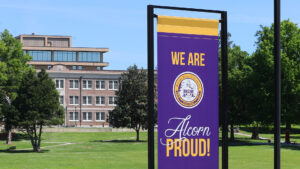 An image of a vertical banner reading, "We are Alcorn proud!" with Bowles Hall and the Walter Washington Administration Building in the background. This image is used as a Zoom background.