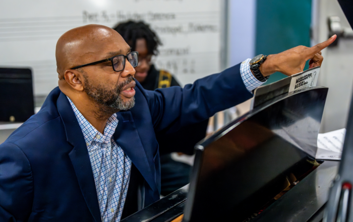 Dr. Sean Daniels in blue suit sitting behind the piano teaching.