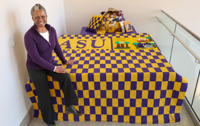 Dr. J. Janice Coleman, wearing a purple cardigan, sits atop here Alcorn-themed quilt.