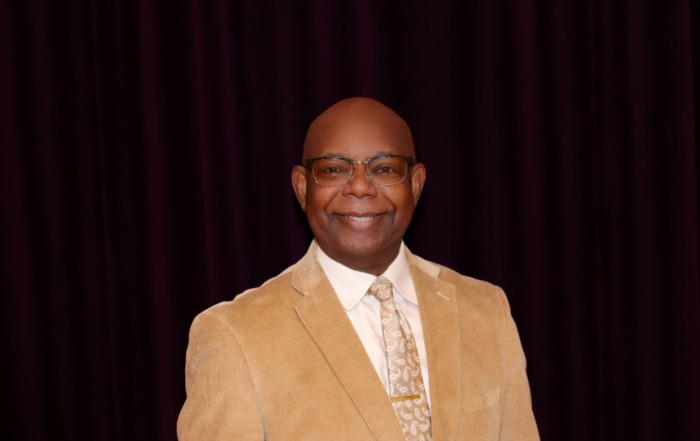 Tony Gordon, assistant professor of music and university organist at Alcorn State University, smiles wearing a tan blazer, white dress shirt and patterned tie.