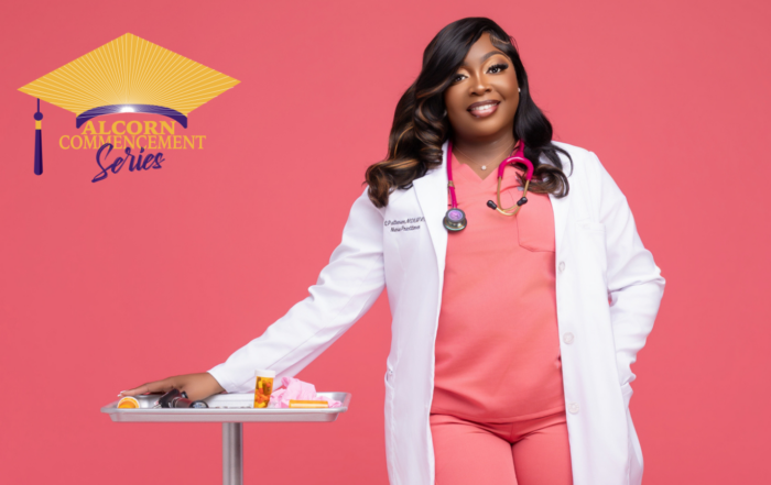 Shantwana Patterson, MSN, FNP, stands confidently in a professional photo shoot setting against a solid pink background. She is wearing coral scrubs, a white lab coat with her name and title visible on the chest pocket, and a pink stethoscope around her neck. She leans with one arm resting on a silver medical tray stand that holds prescription bottles and medical supplies. She is smiling warmly at the camera. Her name tag reads "S. Patterson, MSN/FNP, Nurse Practitioner."