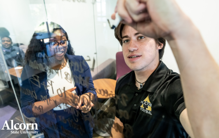 Alcorn State University students collaborate at a glass whiteboard during a study session, with the Alcorn State University logo displayed in the lower left corner.