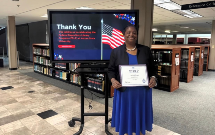 Danielle Terrell, director of the Natchez Library Learning Resource Center, smiling with award in blue dress and black jacket.