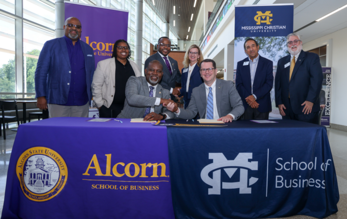 Alcorn State University and Mississippi Christian University leaders shake hands at a signing table after finalizing a Memorandum of Understanding for a 4+1 accelerated Master of Accountancy program, with Alcorn and MC School of Business banners displayed behind them