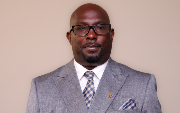 Renardo Murray, newly named dean of graduate studies at Alcorn State University, in a formal headshot. He wears a gray suit, a white shirt and a blue-and-tan checked tie, with a gold Alcorn "A" lapel pin.