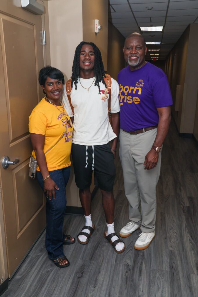 Dr. Tracy M. Cook, in a purple Alcorn "SOAR" shirt, and his wife, Dr. Crystal Cook, in gold, stand with their son, Casey, in a residence hall hallway on Move-In Day.