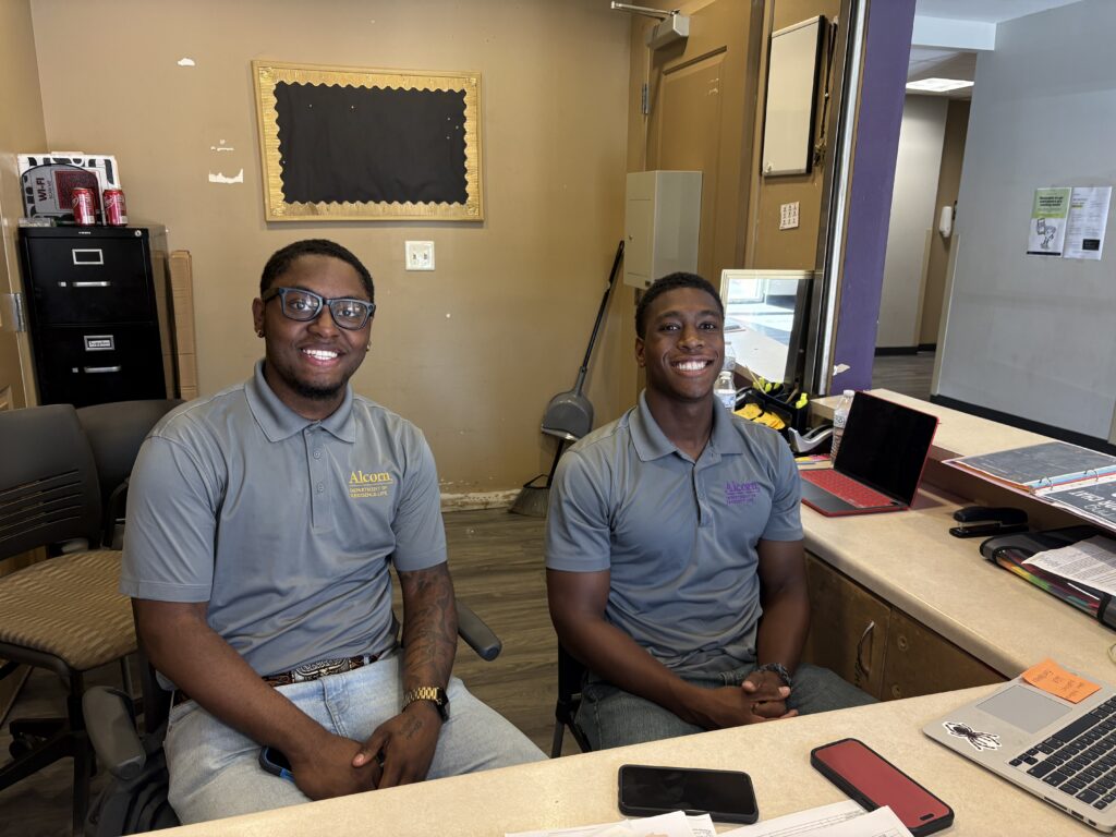 Two resident life staff members in gray Alcorn Department of Residence Life polos sit at a front desk during Move-In Day.