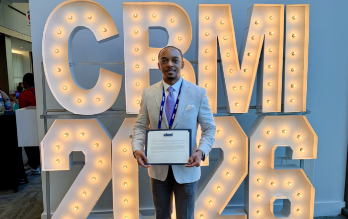 Casey Mock holds his CBMI certificate in front of lit "CBMI 2026" marquee letters at the University of Kentucky.