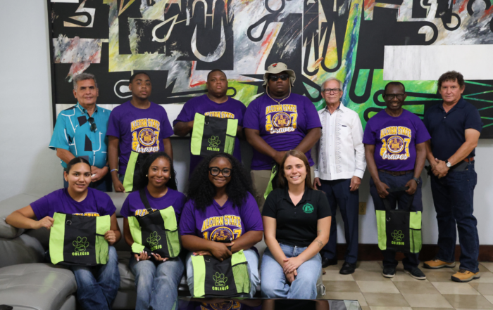 A group of Alcorn State University students and faculty pose together indoors in front of a large abstract mural. Several students wear purple "Alcorn State Braves" T-shirts and hold green-and-black tote bags reading "Colegio." Host faculty in casual dress stand alongside them.